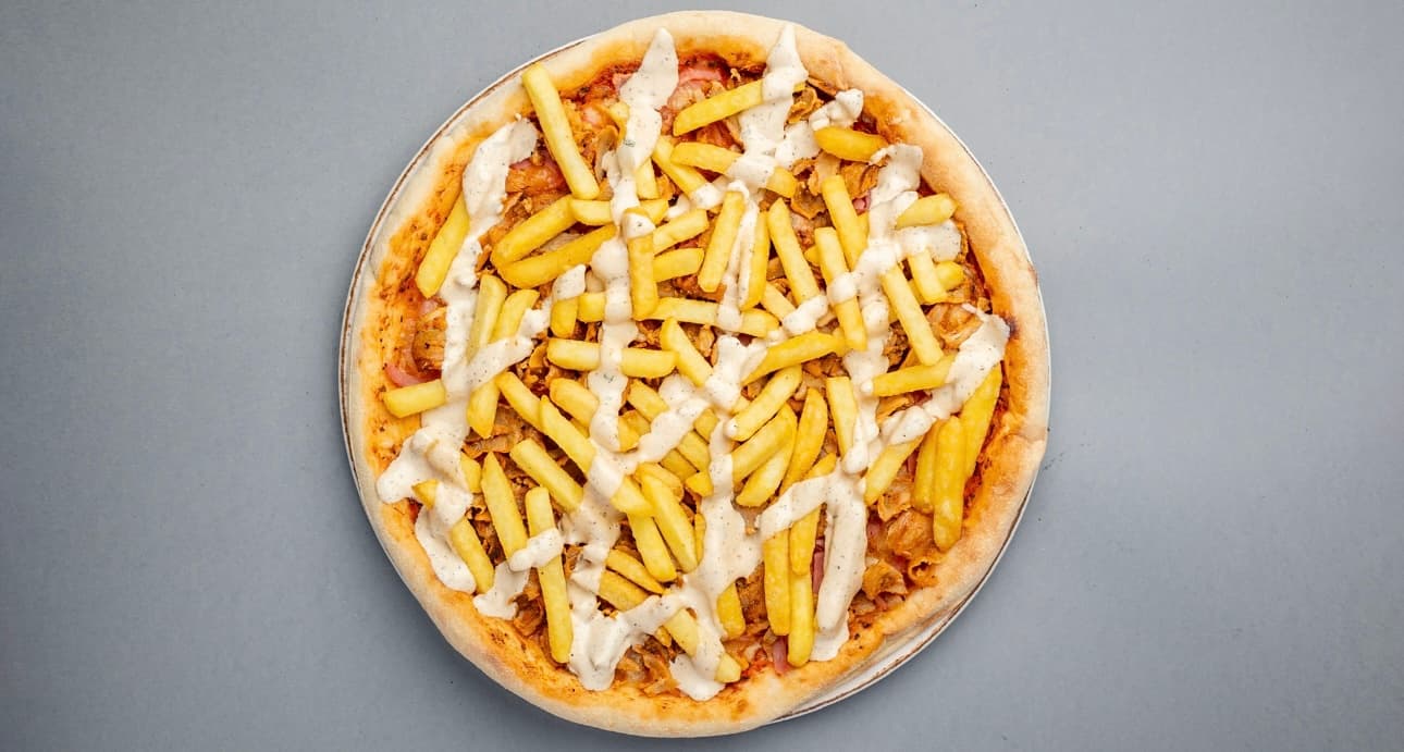 Kebab pizza topped with golden french fries and a drizzle of creamy white garlic sauce.