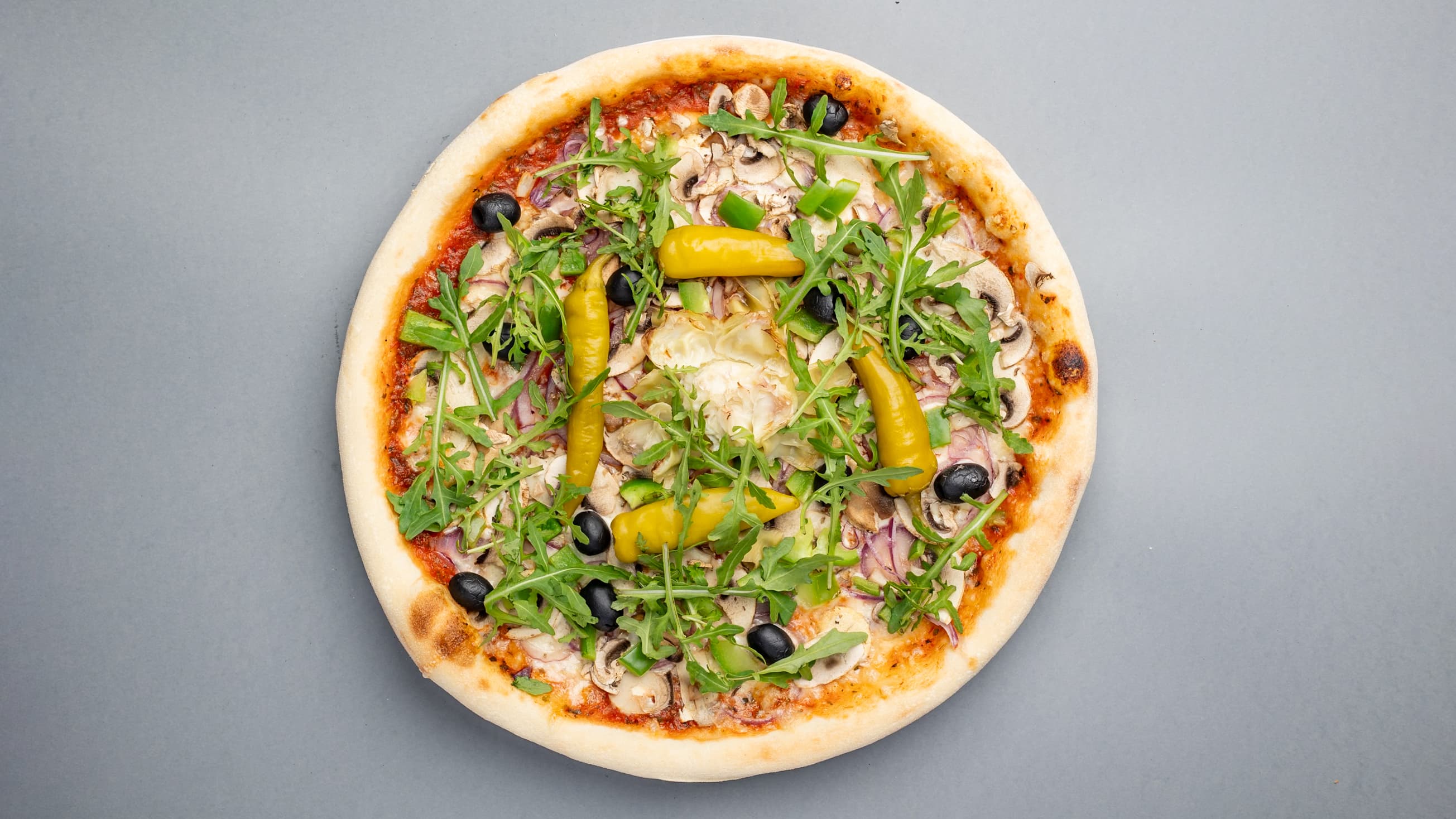 Vegetarian pizza topped with fresh arugula, black olives, mushrooms, and whole yellow chili peppers.